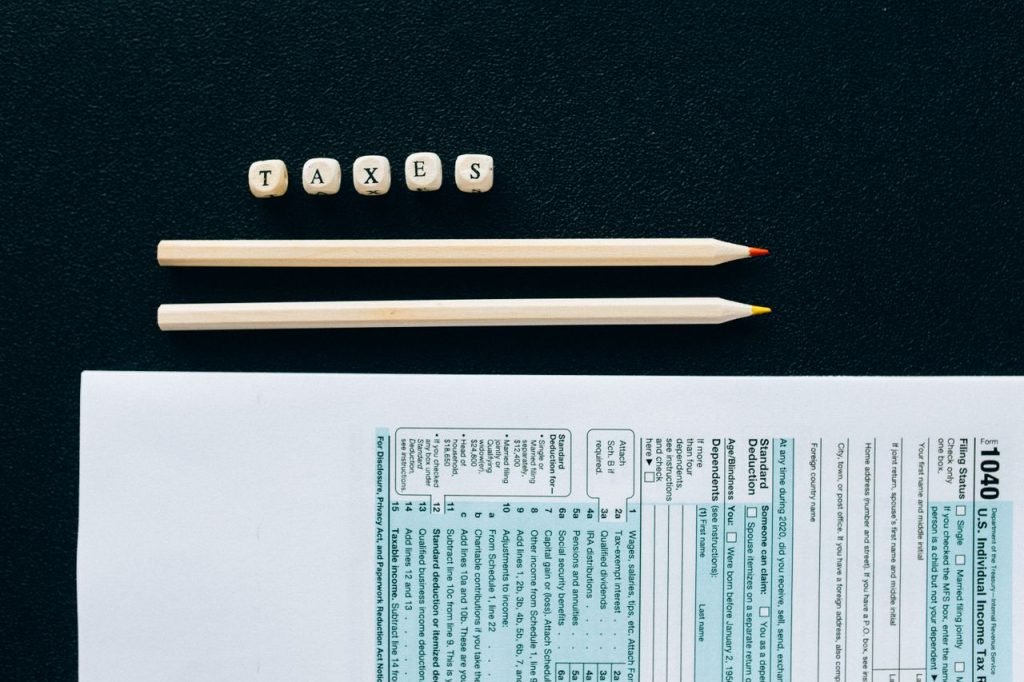 Flat lay of 1040 tax form with pencils and TAXES blocks on black background.